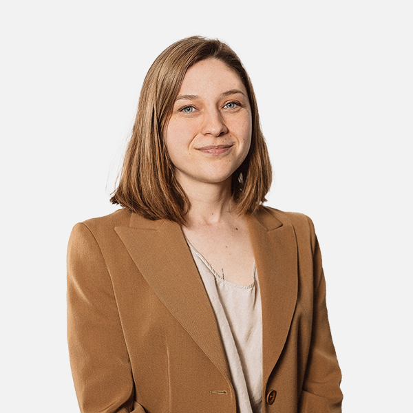 Joline Siegwarth mit schulterlangen, glatten, hellbraunen Haaren trägt einen eleganten, braunen Blazer über einer cremefarbenen Bluse. Sie blickt freundlich in die Kamera vor einem weißen Hintergrund.